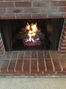 Hargrove radiant heat Cross Timber gas logs inside wood burning fireplace.